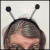 emceeaich: A woman in glasses with grey hair, from the eyes up, wearing a hairband with 'insect antenna' deelie-boppers (bugmaster)