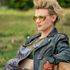 squint13: Jillian Holtzmann, from Ghostbusters 2016, sitting on a benc, wearing her yellow goggles and black leather jacket, looking focused (Default)