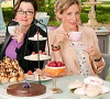 technocracygirl: Mel and Sue, from Great British Bake Off, sitting behind a table with a lot of different pastries (cooking)