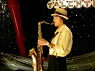 noxelementalist: Dustin Brooks from Power Rangers Ninja Storm, dressed in black pants, yellow-long sleeve, and with a fedora on his head; he's playing a saxophone on a TV talent show stage (Dustin Brooks)