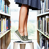 lirazel: A girl in a skirt stands on her toes on a stool to reach a library book ([books] natural habitat)