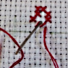 ilyena_sylph: a circle of red cross-stitch stitches, the bottom two unfinished, with the needle just starting through the cross of an unfinished one (Photos: cross-stitch)