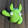 ziz: A small green sculpted figurine with an earnest grin, big ears or horns, and huge low-set eyes, looking up at the camera and waving. (Default)