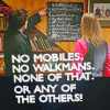 obstinatecondolement: Bernard Black and Manny Binaco from Black Books pictured from behind in a wide shot. Bernard is pointing towards a blackboard. The image is captioned, "No mobiles, no walkmans, none of that, or any of the others!" (none of that)