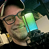 em_kellesvig: David Hewlett grinning behing a blue/green lighted microphone (dhmic)