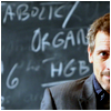 highlander_ii: House sitting in front of a chalkboard with some writing on it ([House] 004)