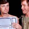 luredin: A naked Hawkeye standing with his lunch tray over his chest as Trapper looks on. (M*A*S*H: Hawkeye (Naked))