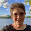 jesse_the_k: Smiling white woman, thick glasses, in front of big lake, deep blue sky and fluffy clouds (JK 66 loves up north)