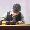 sakanawords: picture of a man writing at a desk (luofei-writes-desk)
