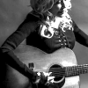 yarnofariadne: a black and white image of dolly parton, with long wavy blonde hair falling over her shoulders. she's wearing a dark button-up shirt, and looking down at the acoustic guitar she's playing. (music: with the stars in her eyes)