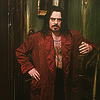 yarnofariadne: jemaine clement as vlad in what we do in the shadows. he's wearing an open red coat and posing with one hand on his hip and the other leaning on the banister railing next to him. (film: baby you're cruel to me)