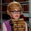 kareila: a lady in glasses holding a stack of books (books)