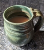 keshwyn: Mug of tea, glazed in green and brown, on a blank quartz countertop, in a sunbeam (tea)