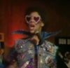 thetubfullofcats: young brown man with an afro wearing glittery heart shaped sun glasses and a jacket with a lot of glittery patches and the most awful and wide collar you have ever seen. he is standing in front of a microphone (bby Lister -- Red Dwarf)