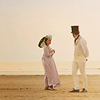 shallowness: Esther holding a parasol and Babbington standing on the beach twisting a little to look at each other (My Lady Disdain on the beach)
