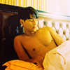 mizerable: a character from thai BL drama kinnporsche; a toned thai man shirtless in a large bed with an elegant headboard (glowing;)