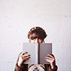 yarnofariadne: a brown-haired white woman holding up a grey book in front of her face. (misc: you could read me anything)