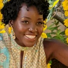 yarnofariadne: lupita nyong'o, a black woman with short curly hair, smiling brightly against a backdrop of yellow flowers. (ppl: ain't no sunshine when she's gone)