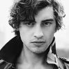 timebethine: A greyscale picture of a white man with curly brown hair; his collar is askew in the wind. He has a serious expression. (Default)