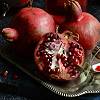 yarnofariadne: a silver platter of pomegranates, one sliced in half, with a sprig of some green plant at the bottom of the platter. (misc: suitcase full of summertime)