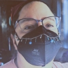 crashmargulies: a white nonbinary person in glasses and a black KN95 respirator mask. They have a silver and blue decorative chain across their mask with star, bead, and evil eye charms dangling from it. (irl me)