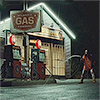 juniperphoenix: Woman in pajamas standing outside a gas station at night, holding a gas nozzle like a weapon (WB: Patricia)
