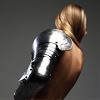 0jack: A blonde woman, bare except for elaborate armour protecting her left arm and shoulder, turns away from the camera. (Naked under armour.)