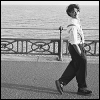 cranky_x_crocus: Grinning woman, short-cropped curly hair, suit and shirt, trouser braces; strutting on pavement in front of an ocean. (Women || Zoë Lewis strutting.)