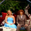 petra: Two women on an outdoor swing, one wearing a strapless dress and one wearing a pants suit. (Suburban Shootout - Butch/Femme)