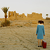 norah: Girl with suitcase, looking out across desert at a fort (travel)