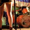 sansets: Z Berg's legs, standing a few feet away from a drum set with The Like written on it (The Like)