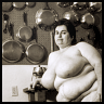 katarik: Naked fat White woman sitting by a kitchen table, pots gleaming on the wall behind her. (Kitchen lives.)