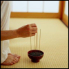 maewyn: a barefoot person in white clothing places one stick of incense with several others in a bowl (incense)