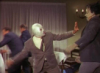 el_enmascarado_de_plata: Santo in a silver full face Spandex mask and brown suit and tie, punching a guy across the room (eject button for the human memory (color)