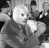 el_enmascarado_de_plata: Santo in a silver full face Spandex mask and suit jacket, clasping his hands and watching something offscreen (watching the terrible musical number (b&)