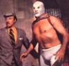 el_enmascarado_de_plata: Santo in a silver full face Spandex mask and some guy in everyday clothes, looking at something off camera to the left (something is coming from the left! (colo)