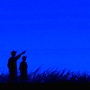 gradient: a silhouette of two people against a deep blue night sky; one is pointing to something (stargazing)