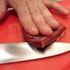 rydra_wong: Fingers holding down a piece of meat (heart) as it's cut with a knife, on a bright red surface. (food -- a slice of heart)