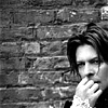 smilingslightly: Black and white photo of David Bowie against a brick wall, looking pensive. (bowie_bw_hand (dorcas_gustine))
