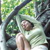 genarti: Young woman perched among tree roots, hanging onto arching root and smiling with closed eyes. ([misc] treehugger at rest)