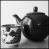 calissa: A black and white photo of a large, dark teapot and a small Chinese teacup with a fish painted on the side (Tea)