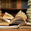 jillian: A pile of books open on a table, surrounded by more stacks and shelves of books. (books)